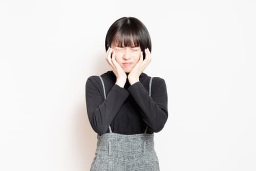年輕香港女子捧著兩頰露出痛苦表情，疑似因智慧齒發炎或牙齦腫脹而引發疼痛。
