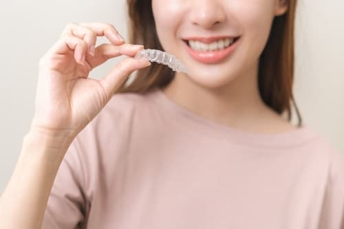 年輕女士手持隱形牙套,展現笑容,自信面對牙齒矯正過程。